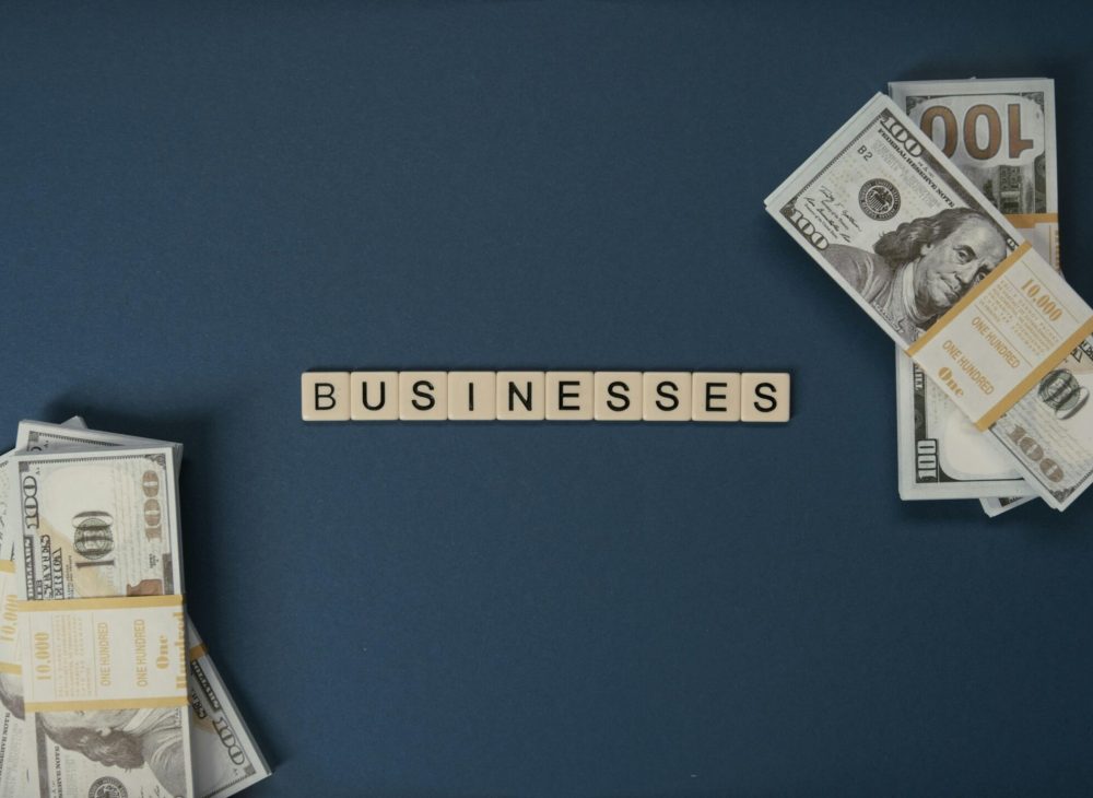 Top view of dollar bills and 'businesses' letter tiles symbolizing financial success.